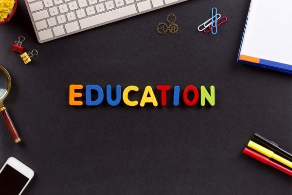 Colorful letters spelling EDUCATION on a dark desk with keyboard, notebook, paperclips, and markers nearby