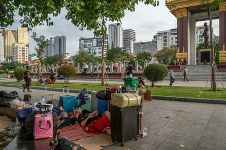 People sit or lie among piles of luggage on the roadside in a city