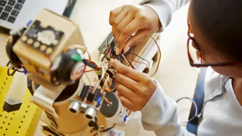 Getty Images A schoolgirl works on the electronics of a robot as part of a school assignment