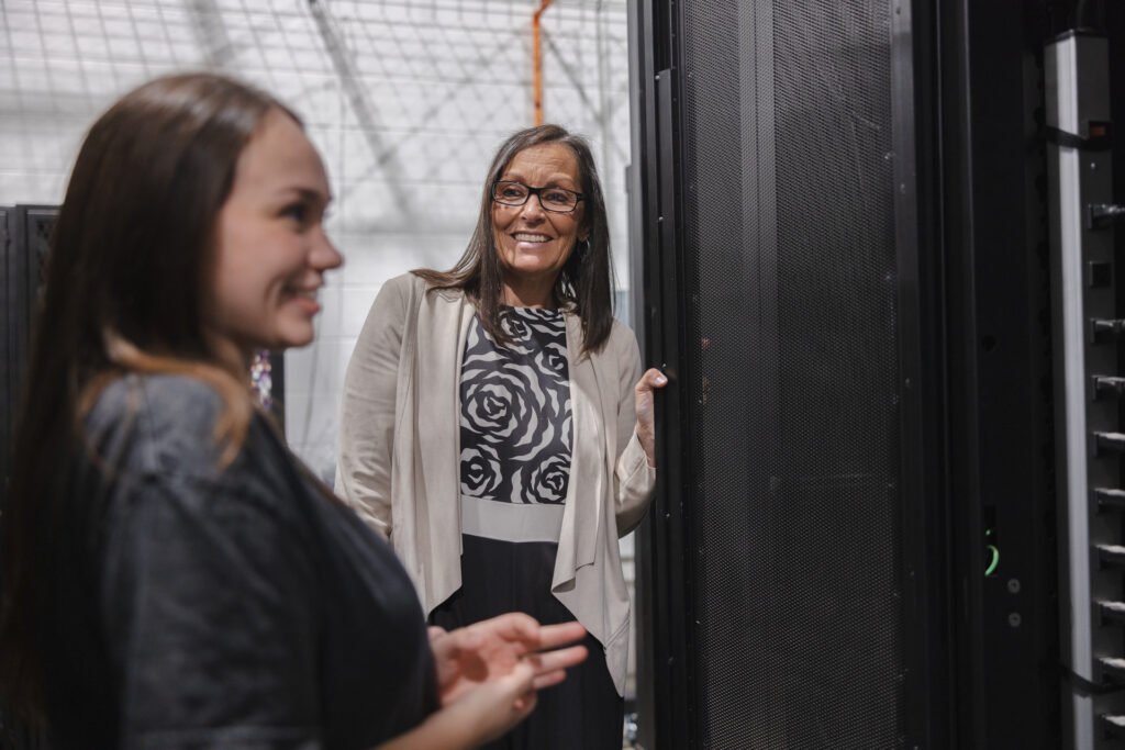 Two dark-haired women examine datacenter equipment in a teaching lab.