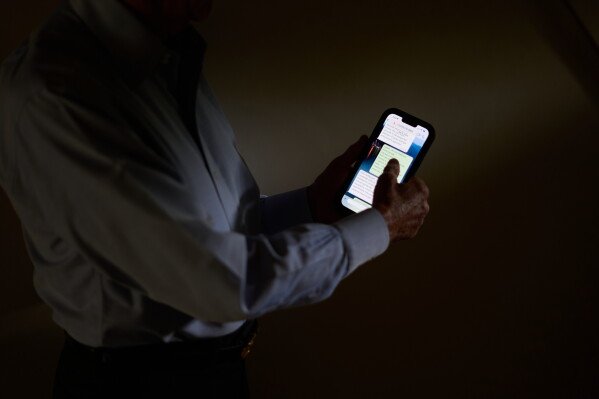 Simon, who was targeted by a scammer that stole $800,000 from his retirement savings and asked not to be identified by his full name because he's too ashamed to tell most of his family about the crime, scrolls through messages with the scammer on his phone, Wednesday, June 17, 2026, at his home in southeastern New York. (AP Photo/David Goldman)